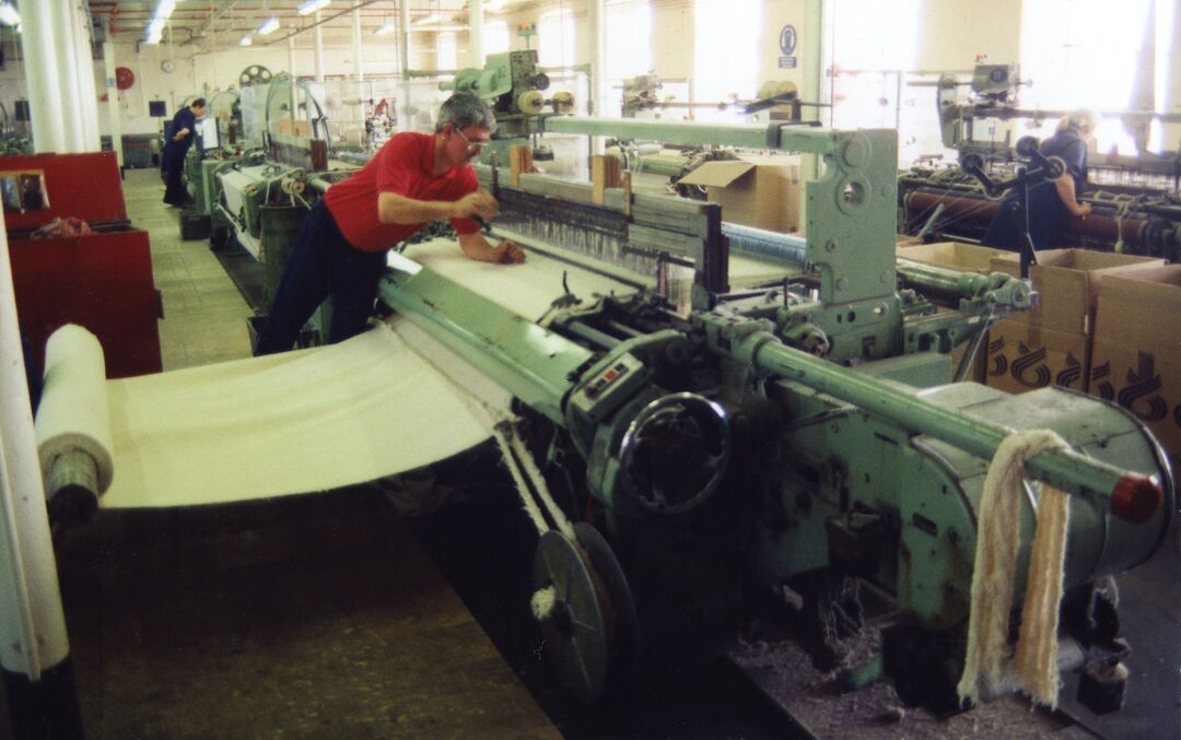 Jute spinning machinery in use, a man is watching the process at the side of the machine while a white fabric is spun out