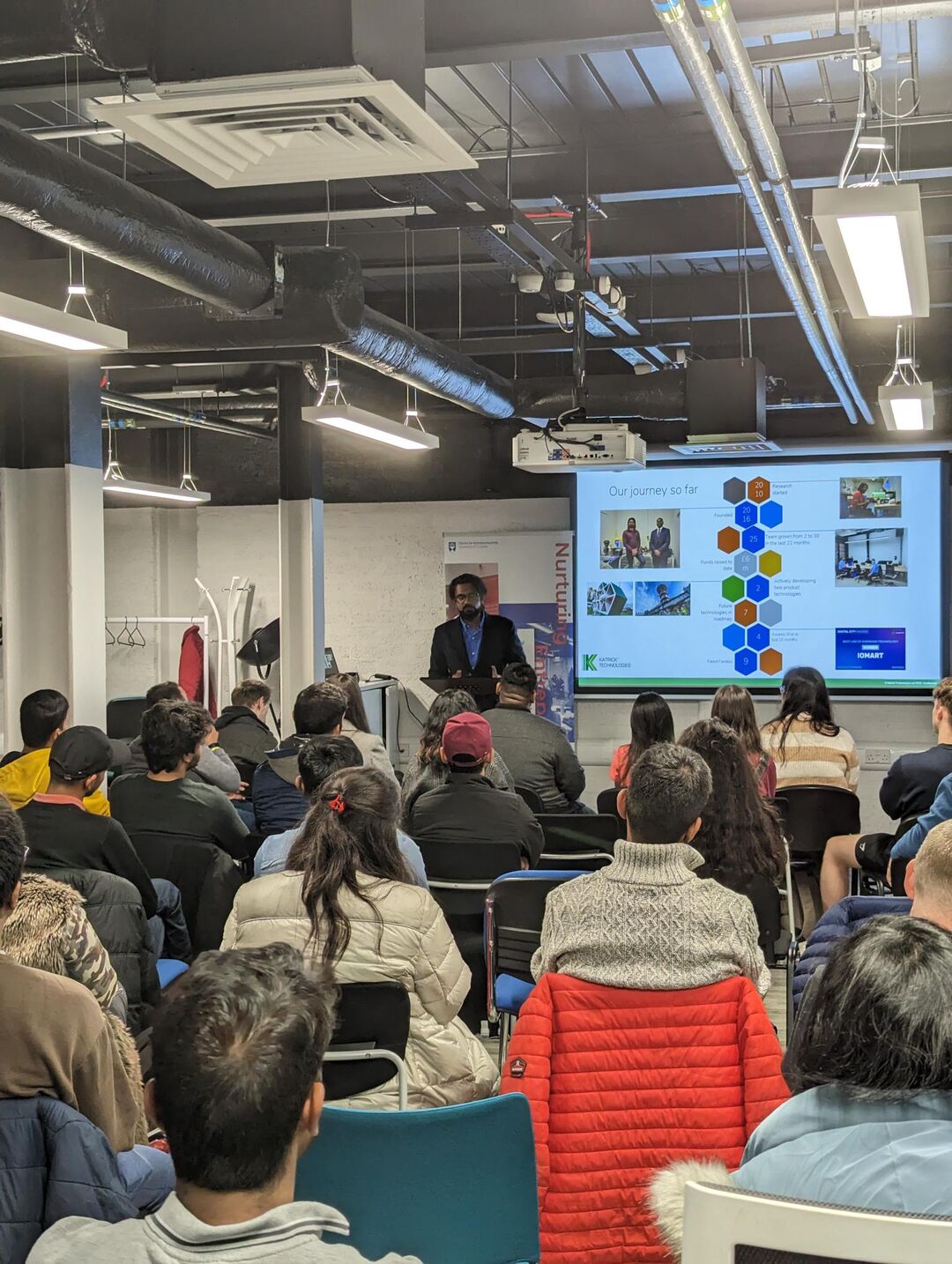 Karthik standing at the front of a room with a view of the crowd in the room