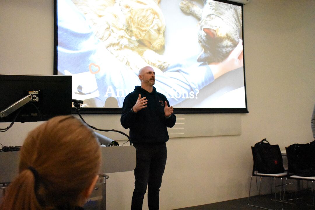 A person standing in front a projector screen with a dog and cat lying down
