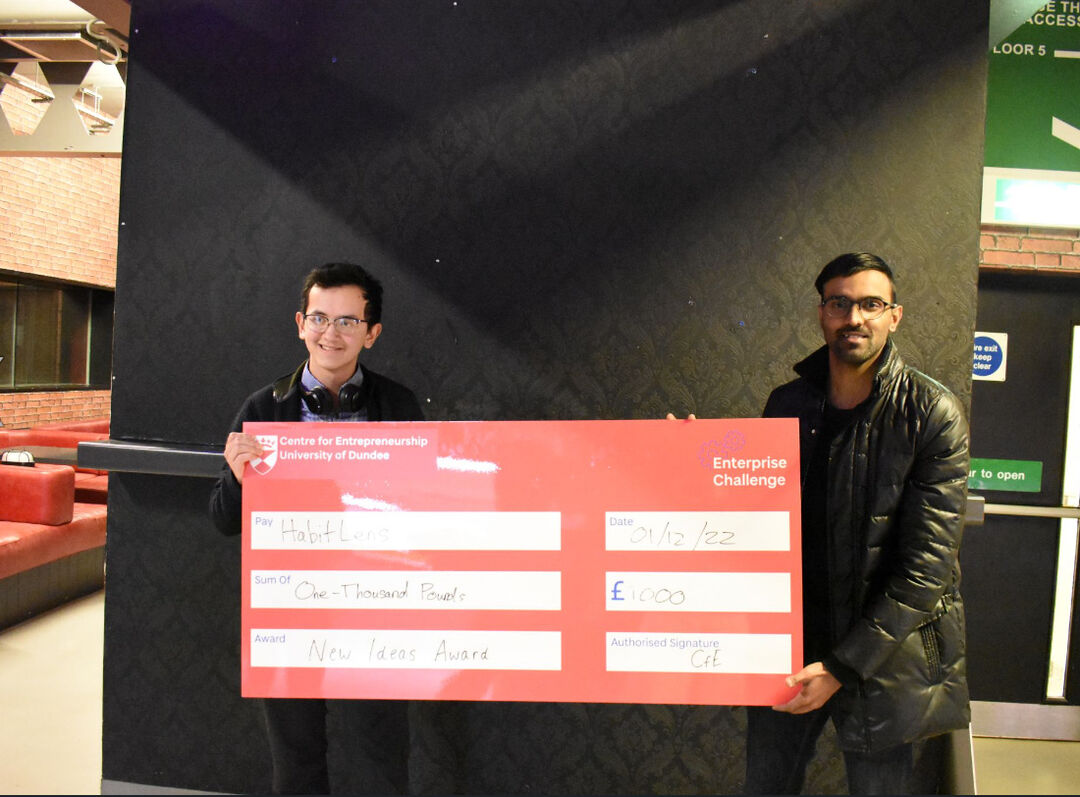 Two people holding up an over-sized cheque for £1000 as winners of New Ideas Award - Enterprise Challenge
