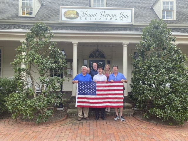 People standing outside of a restaurant in America, holding the American flag.