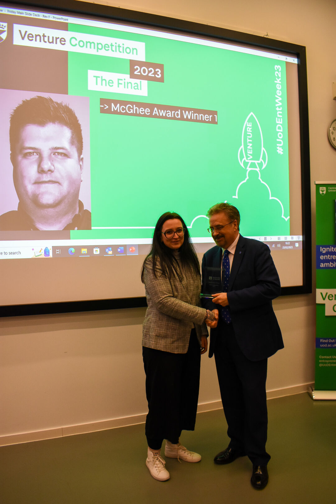 A woman shaking hands with a man, standing in front of a projector screen.