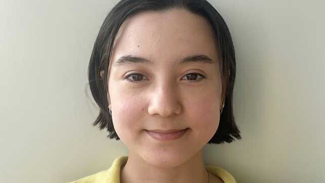 A girl with short dark brown hair, wearing a yellow shirt.