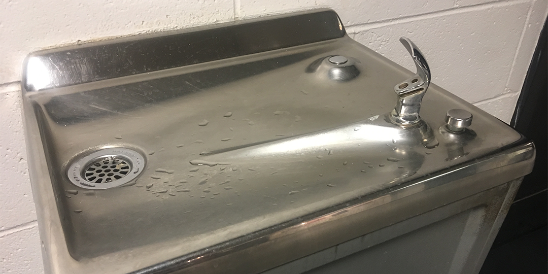 A metal drinking fountain against a white wall 