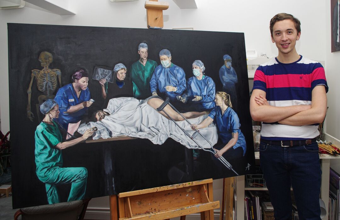 Alastair Faulkner stands beside a large oil painting depicting surgeons at work.