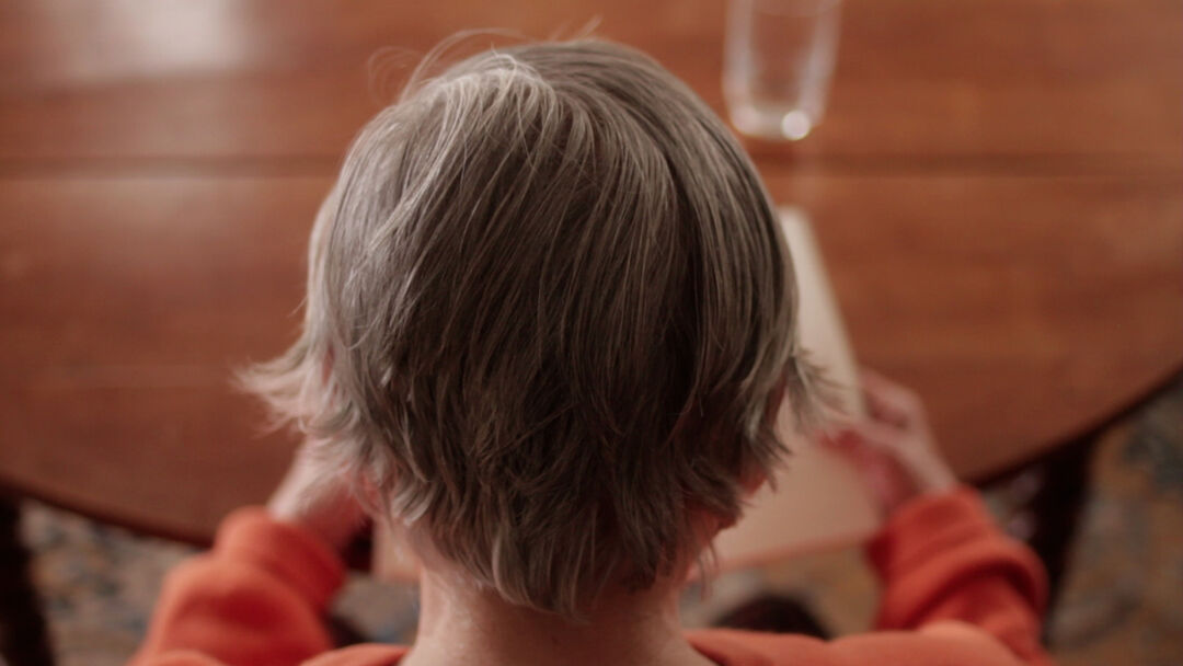 A close up of an elderly woman's head as she reads a book at a table