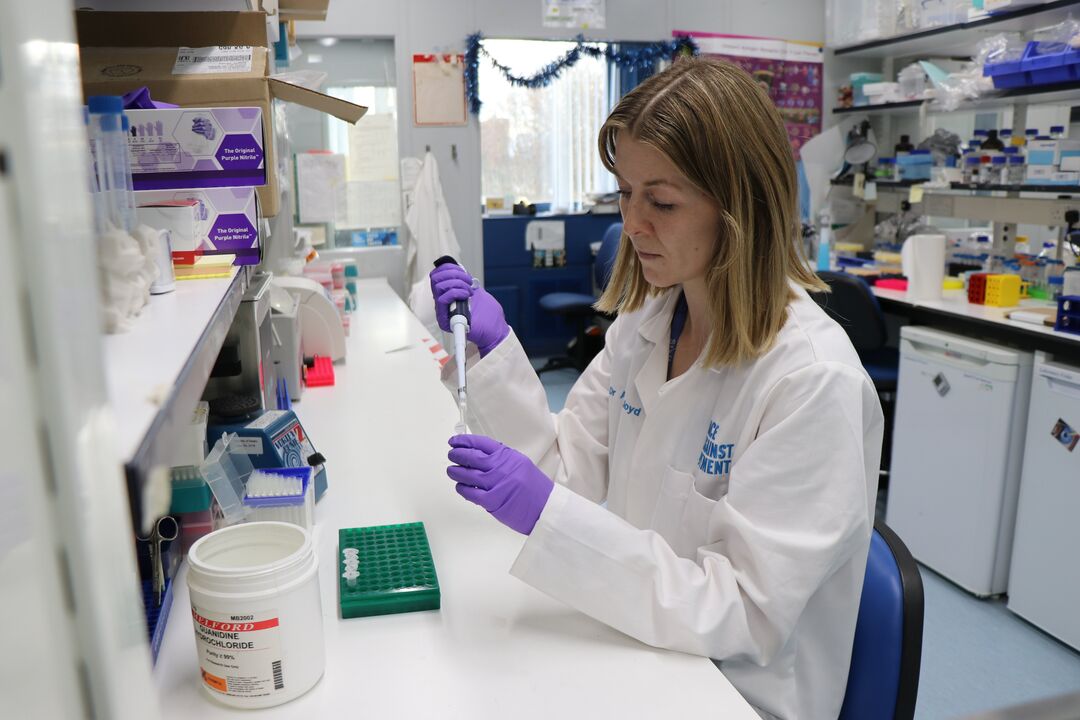Female scientist in white lab coat and purple gloves carrying out science experiments in a laboratory 