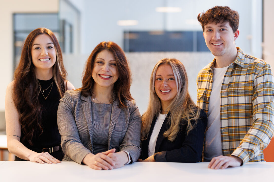 four females and one male standing in a line with their hands on a table in front of them