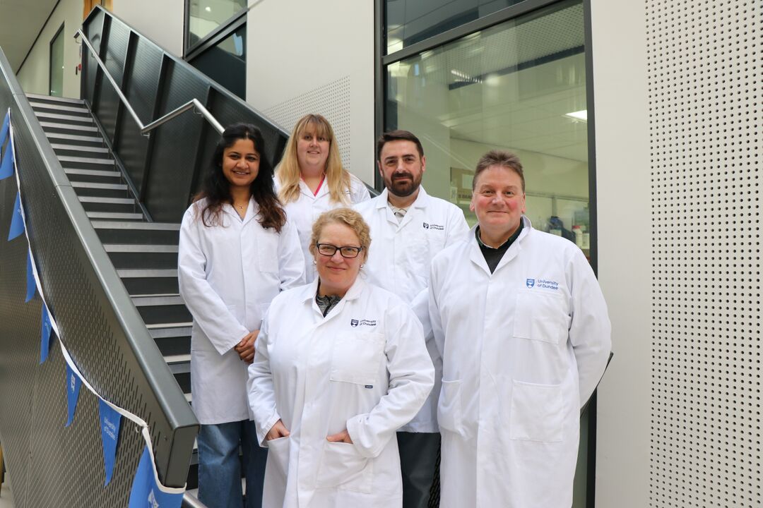 Small group of scientists wearing lab coats standing grouped together at bottom of stairs