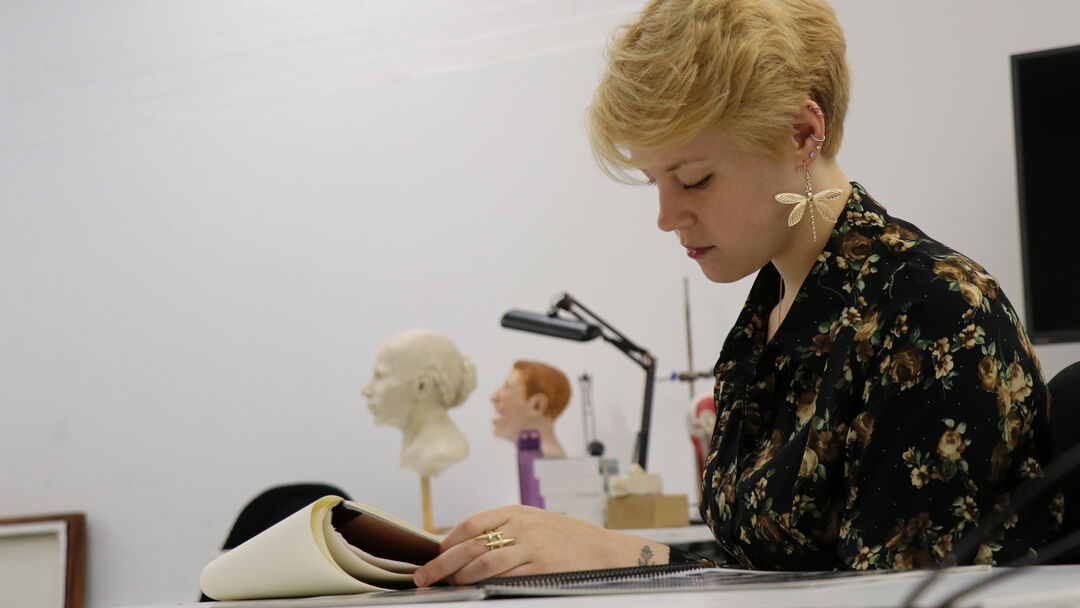 Cydney Davidson sits at a desk while sketching in her notepad