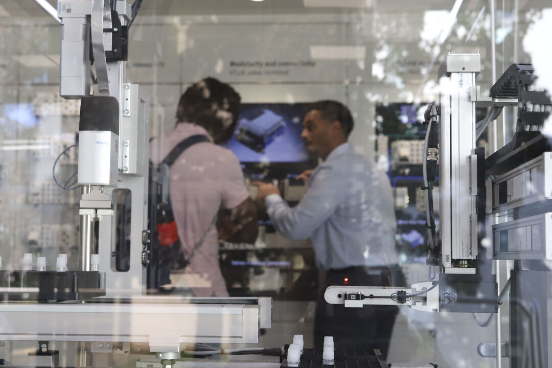 Some machines viewed through a blurred window, two people stand in the background using a piece of equipment.