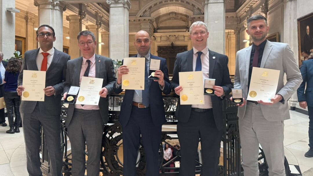 group of five men in suits and ties standing holding certificates looking at camera and smiling
