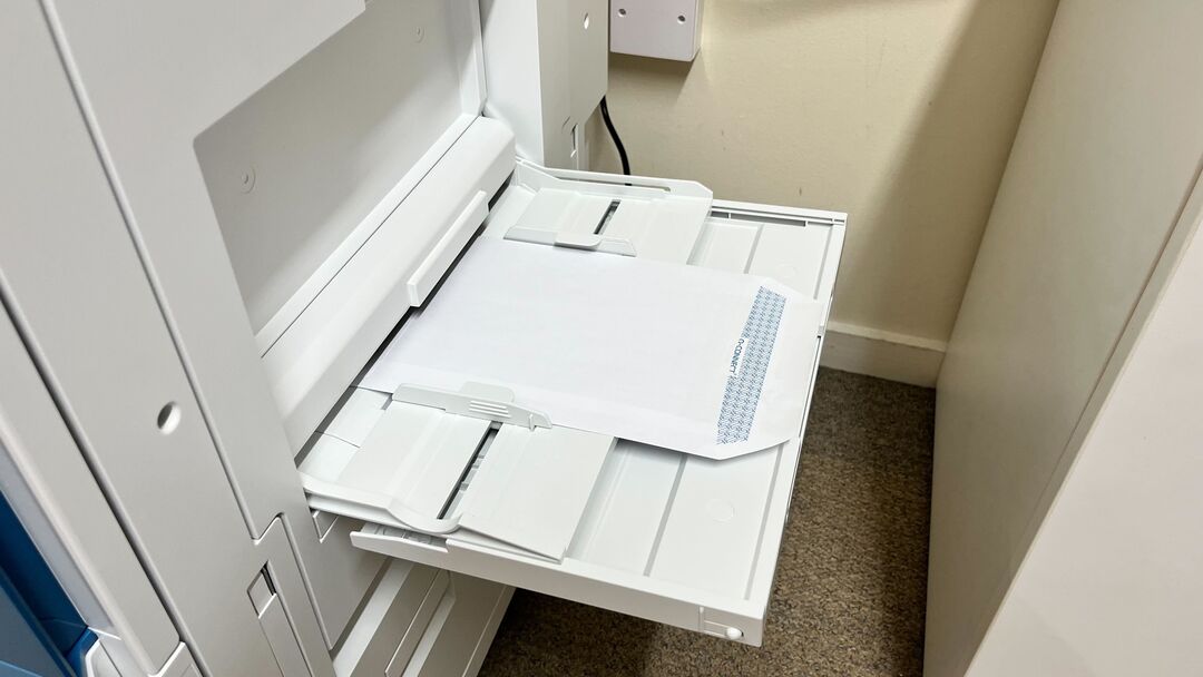 An envelope in the side tray of a printer, the flap is to the right, and the envelope is face down