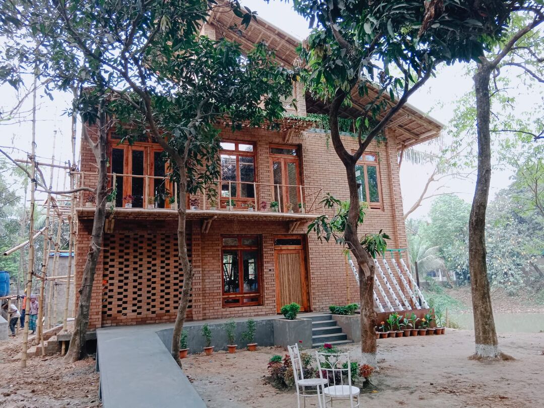 house built from red bricks and bamboo, with trees in front 