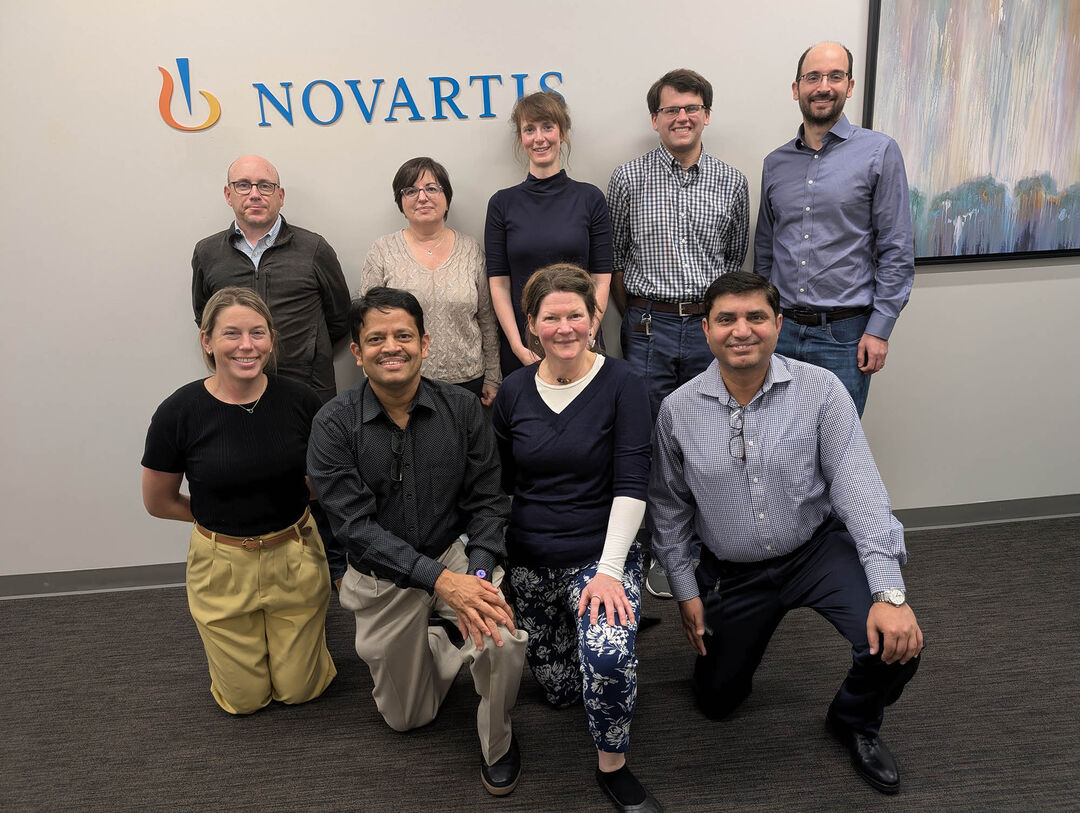 A group of people standing and kneeling together smiling in front of a sign saying Novartis