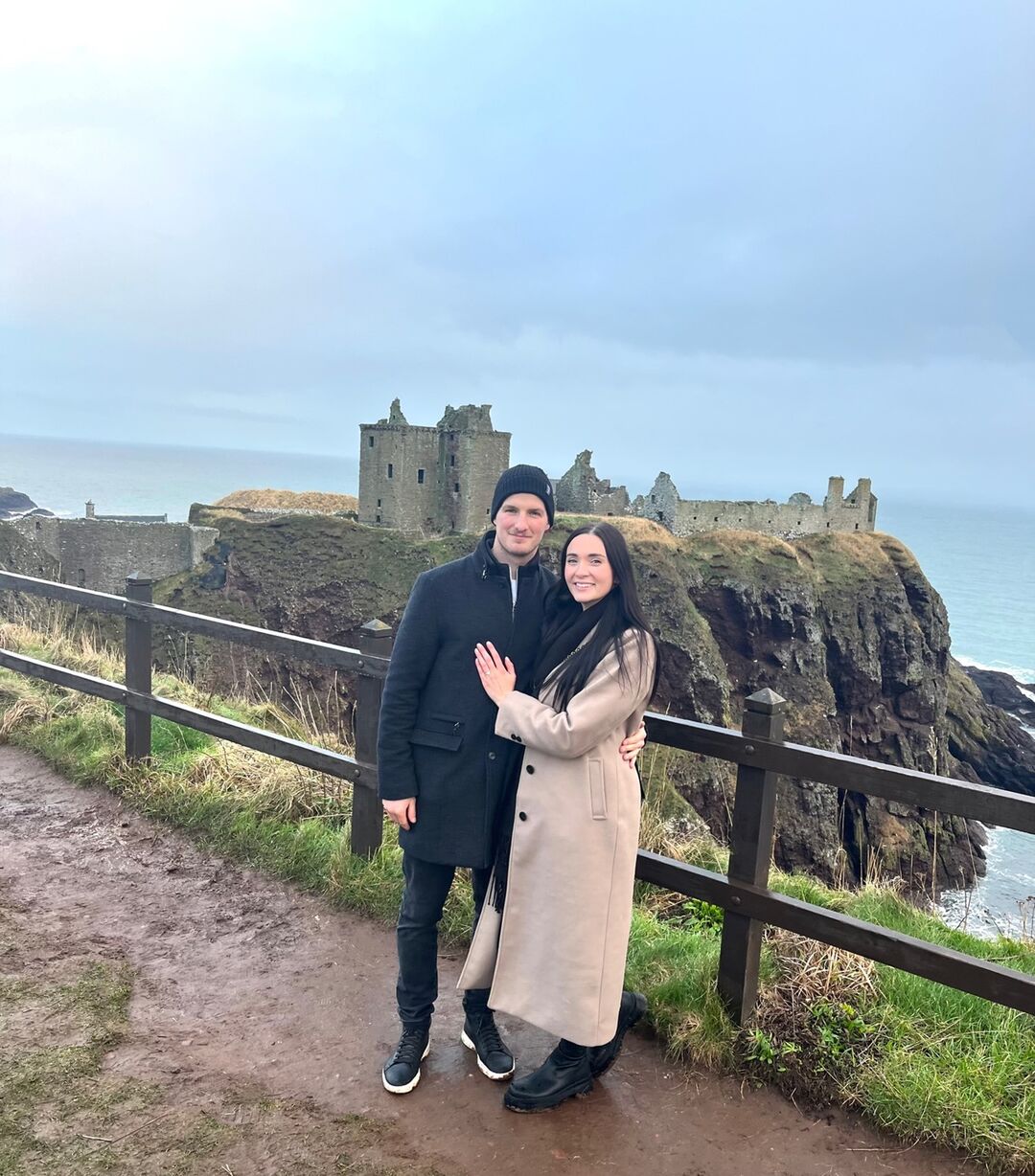 A couple stand close, arms around each other, Dunnottar castle is in the background.