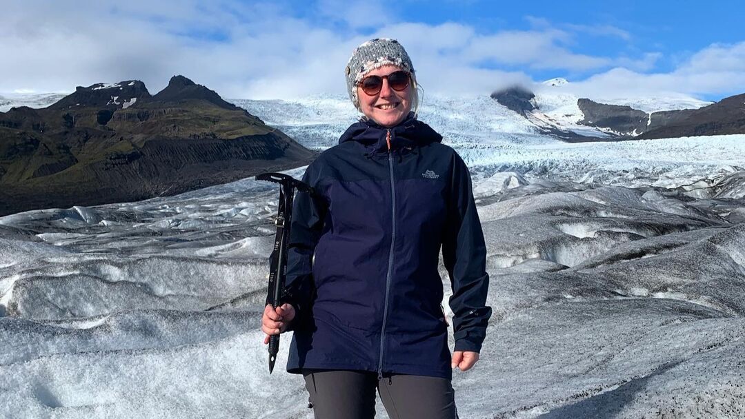 woman standing at snowy mountain holding a climbing axe and wearing outdoor clothing