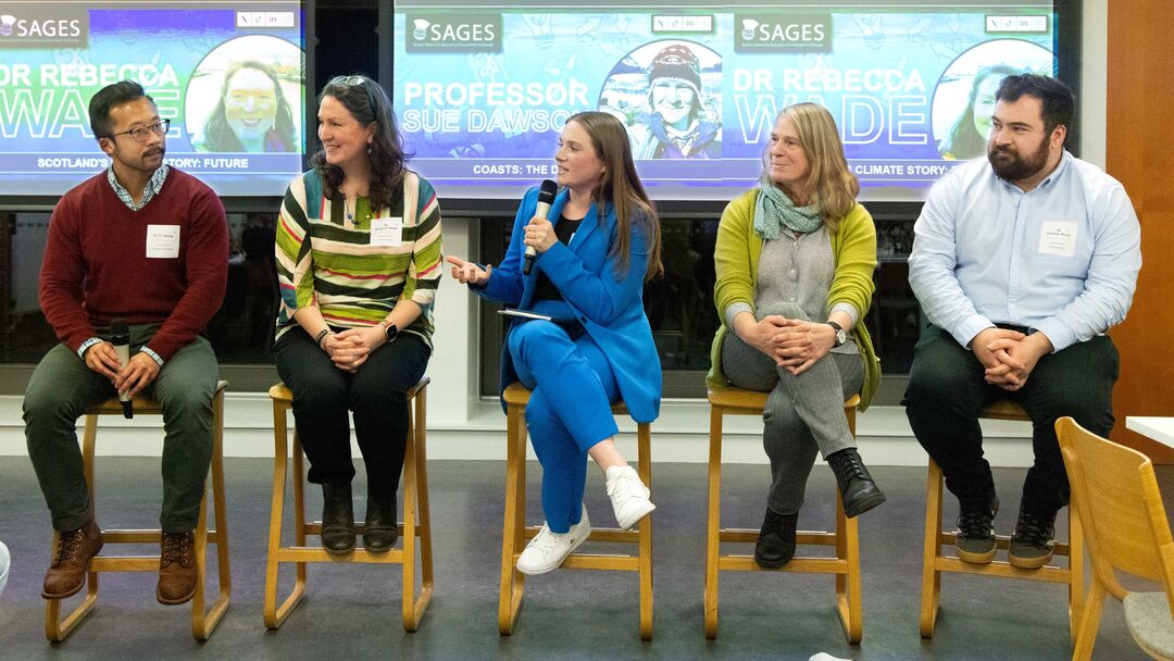 five adults sat on chairs in a line with a large screen behind them
