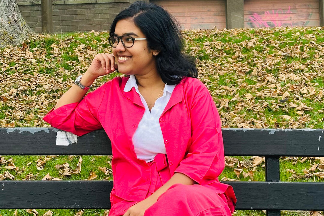 Megha Pradeep Kumar sitting on a park bench with autumn leaves on the grass behind her