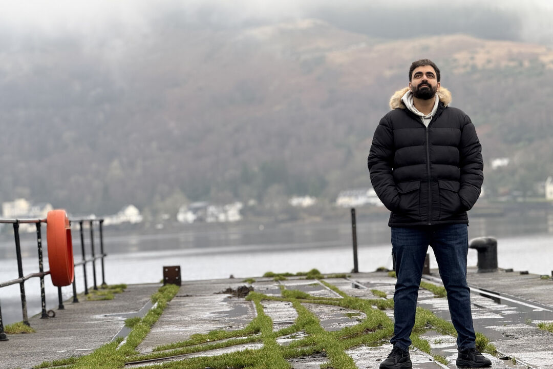 Raghav standing on a pier on a river with hills behind him
