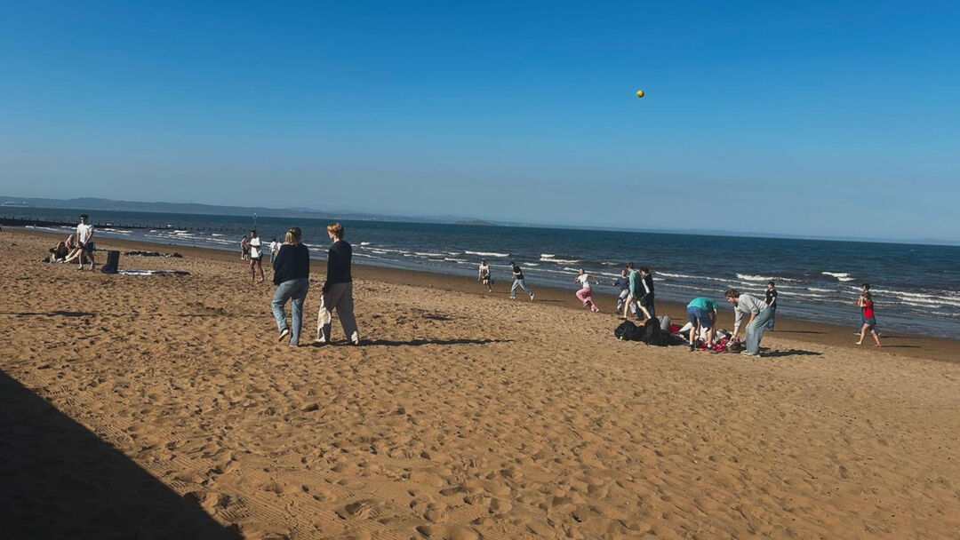 A scatter of people on a sandy beach playing in the sand or taking a walk