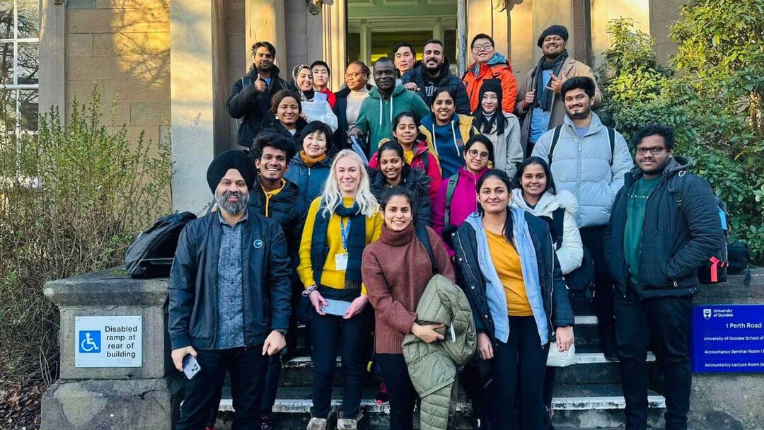 A group of people stand outside a building on the steps leading up to the door.