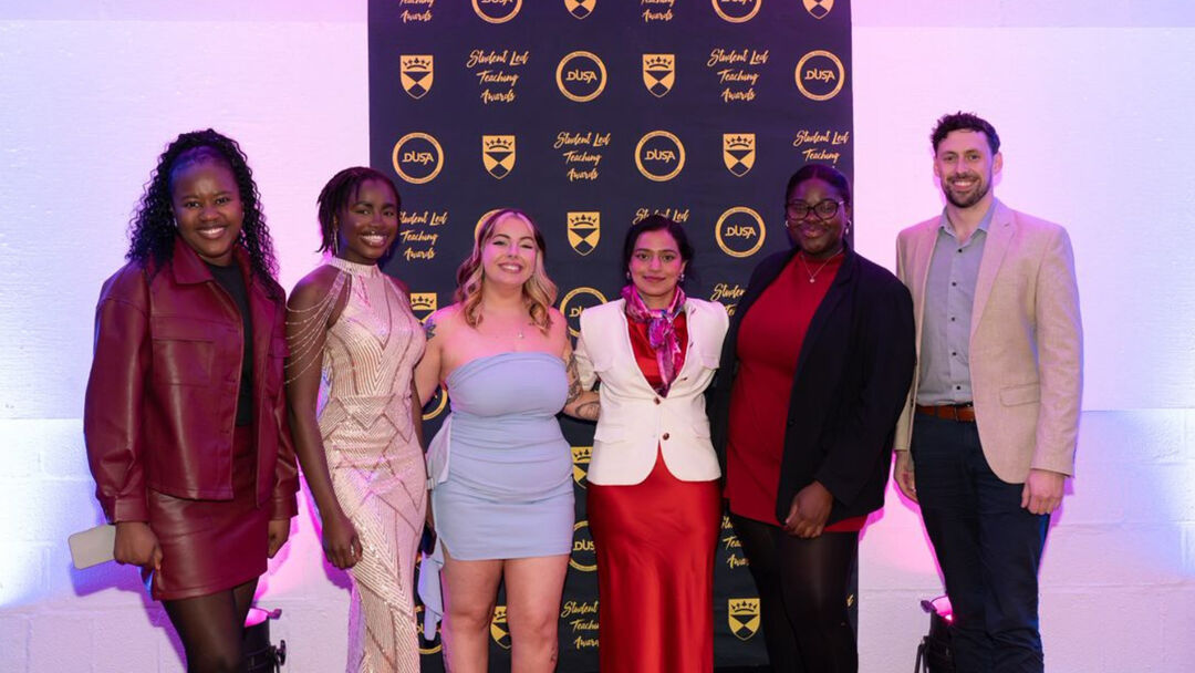 Six students and members of DUSA, standing together and smiling at the camera, wearing formal party clothing