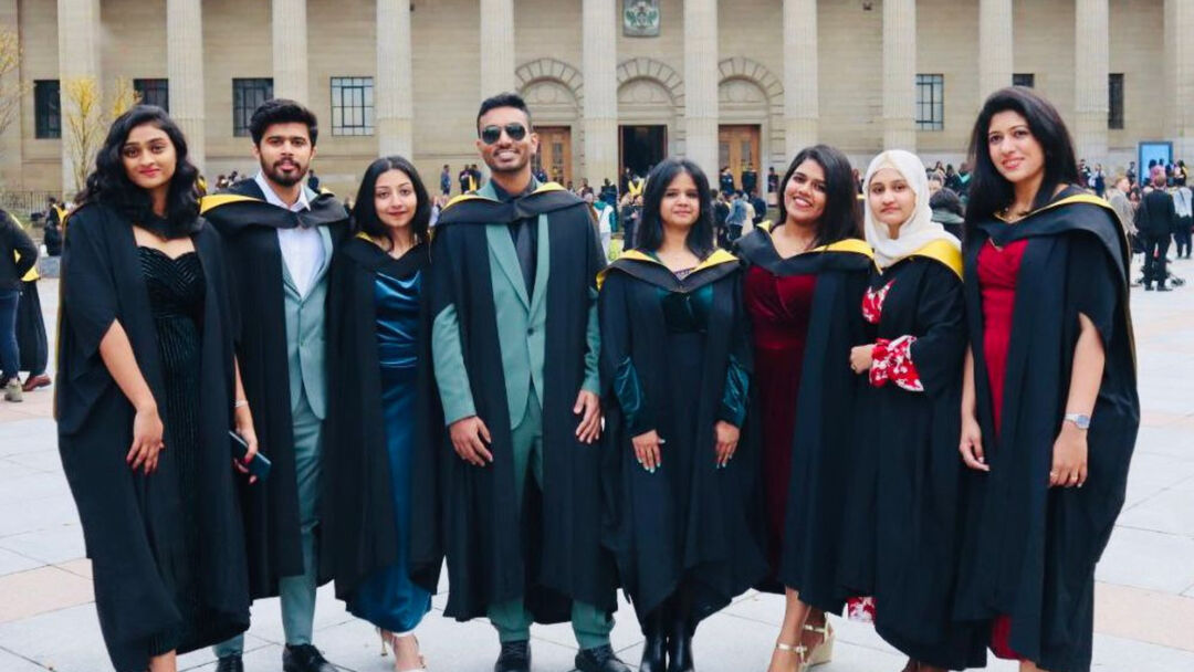 A group of graduates in graduate gowns poses for a photo outside a building