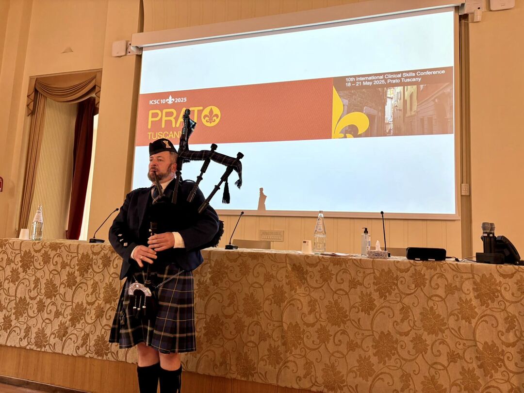 A person stands in front of a presentation screen playing the bagpipes.