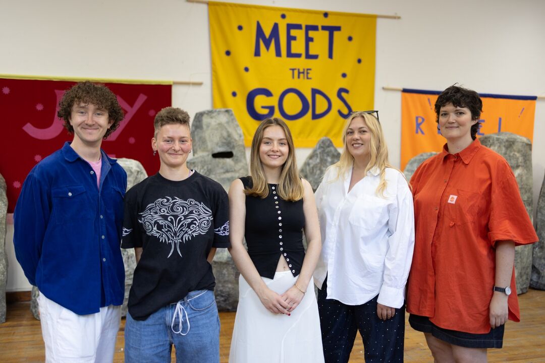 group of people standing in front of Meet the Gods sign	