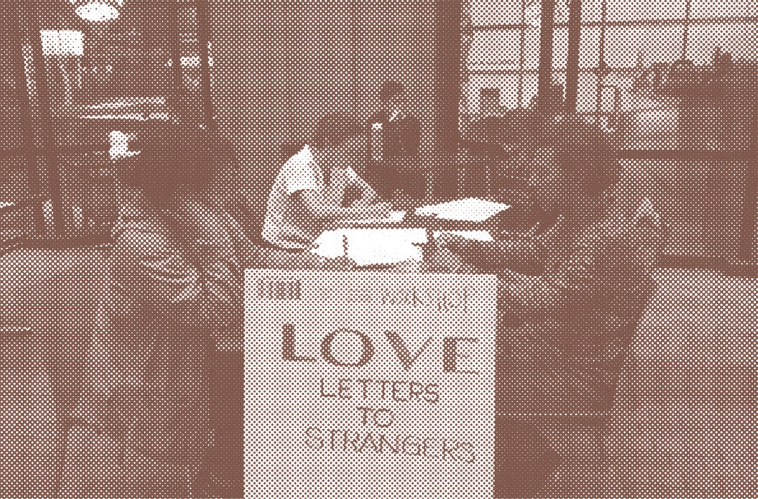 Sepia toned photograph of workshop participants at desks writing. A sign says Love Letters to Strangers