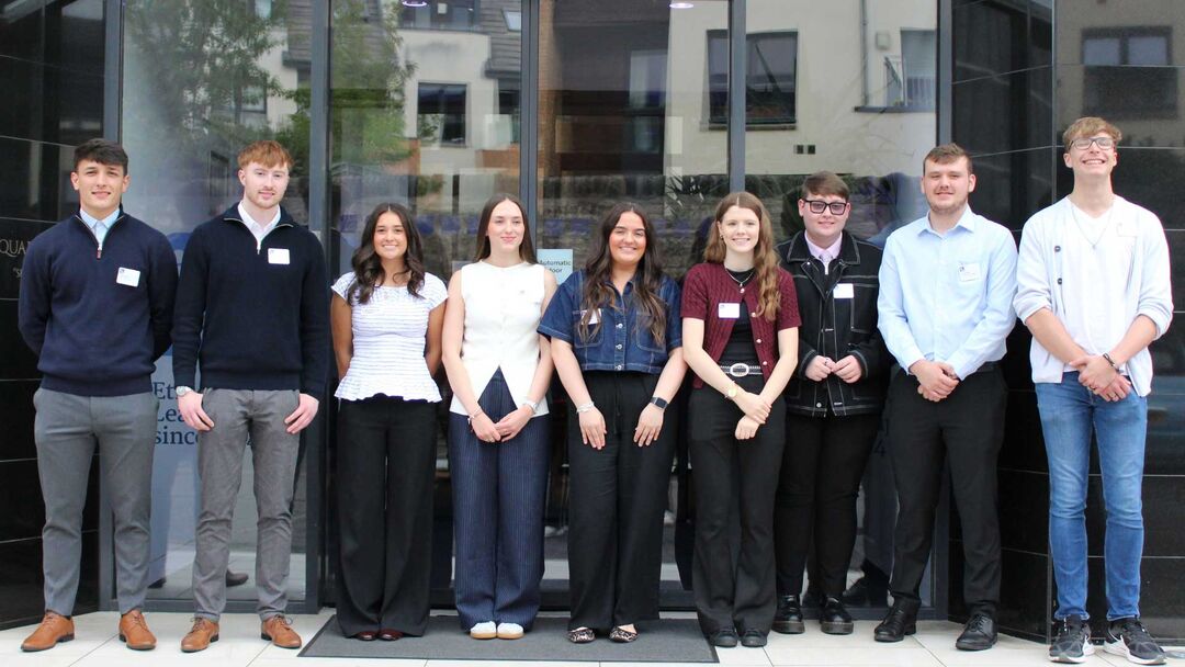 A group of students from all over Scotland stand together in a line, smiling at the camera, there are 11 students in total