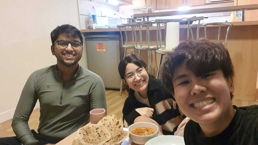 3 students sitting together at the table, eating together and taking a selfie, all are smiling at the camera.