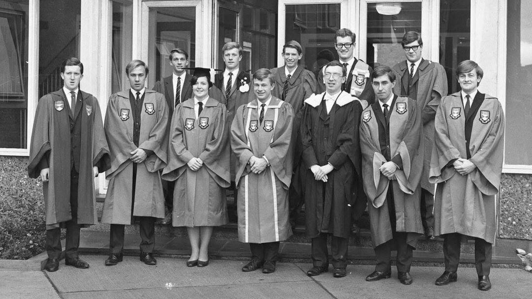 A black and white photo showing Lord George Robertson and other members of the student exec in the 1960s. They are standing outside Belmont Halls of residence and wearing their academic robes