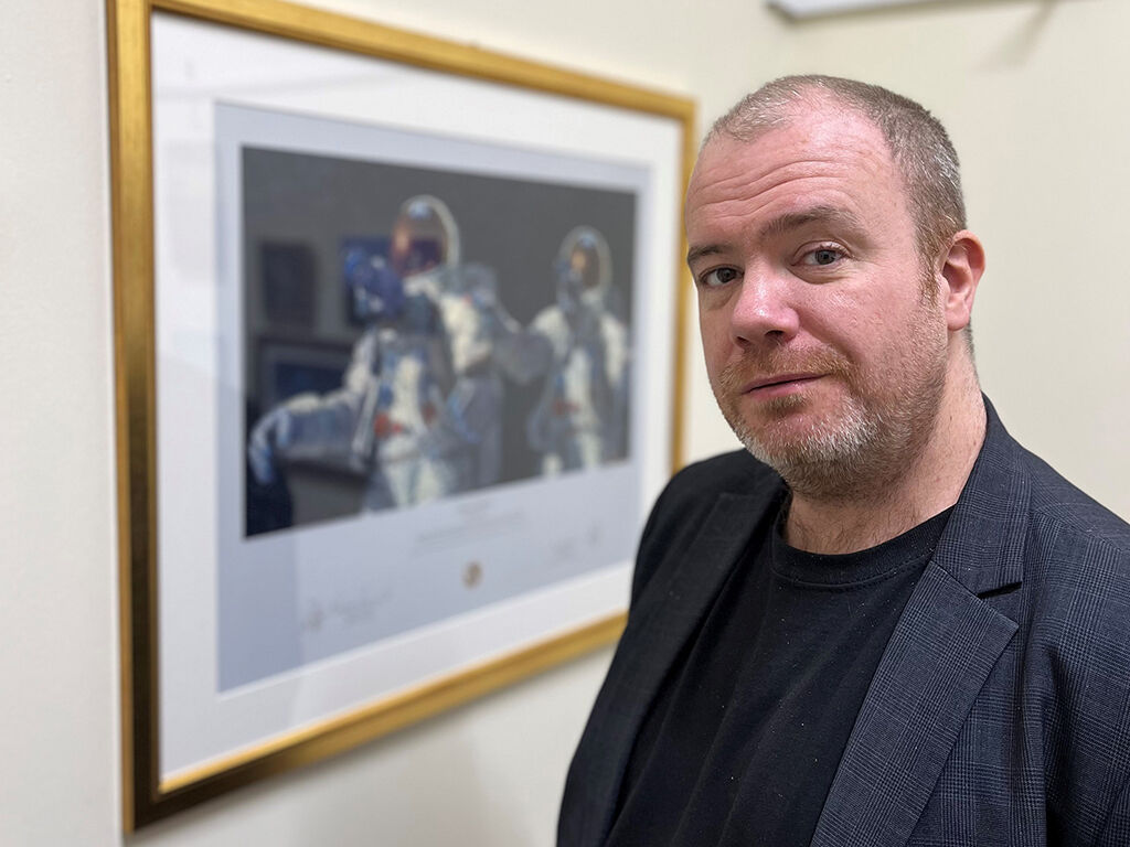 Dr Simmonds standing infront of an image of astronauts