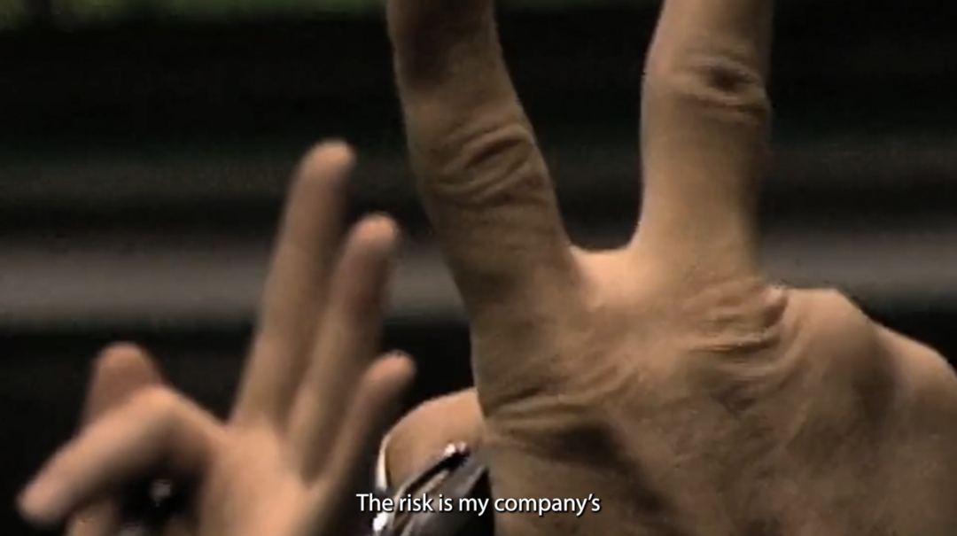 film still. Close up of fingers and hangs held high in the air with caption 'the risk is my company's'