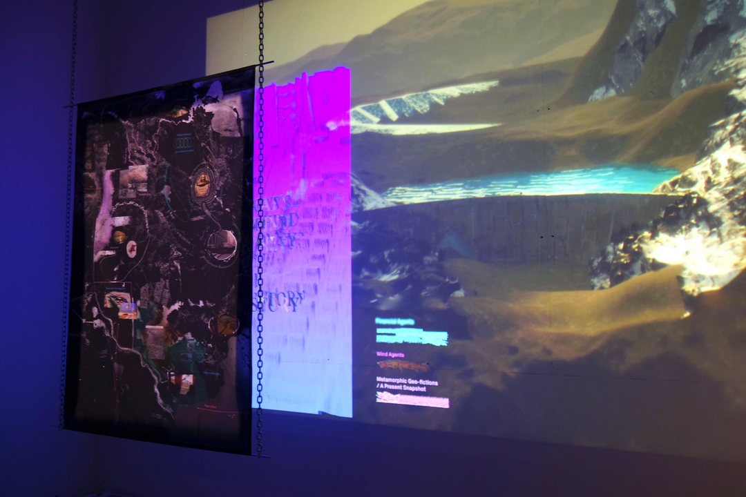 exhibition view, digital projection of a mountain landscape are broken by hanging sheets of textiles and tracing paper