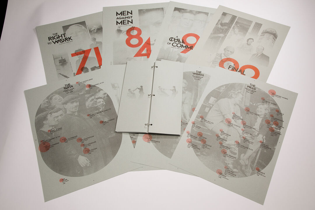 A selection of posters spreadout on a table showng numbers in red and black and white photos as part of the Master Showcase exhibition